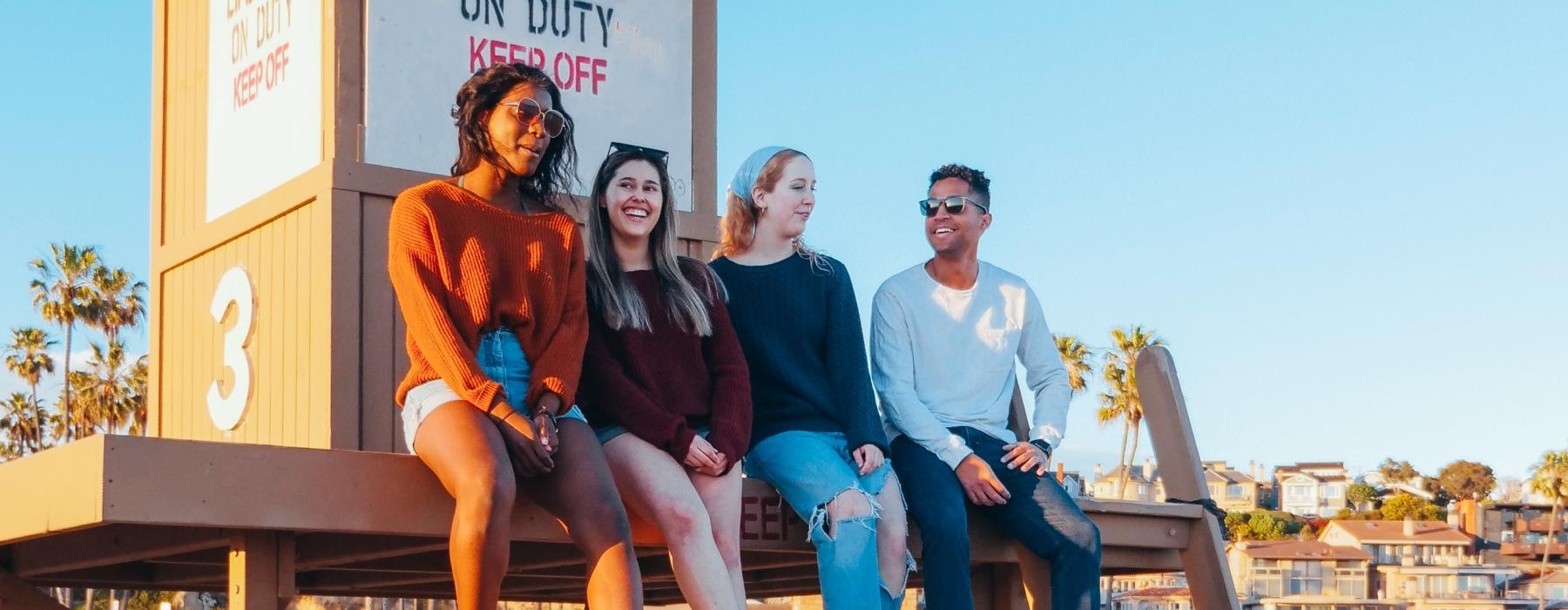 a group of people sitting on a wooden bench on a beach